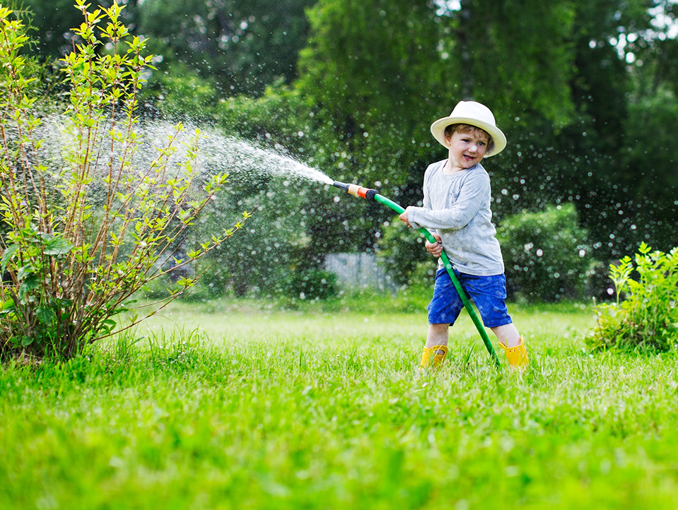 Kind bewässert den Garten mit einem Gartenschlauch